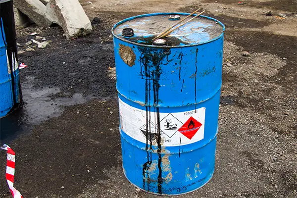 Blue hazardous waste drum with flammable and corrosive hazard signs, located on an industrial site in the UK showing signs of leakage (2025).
